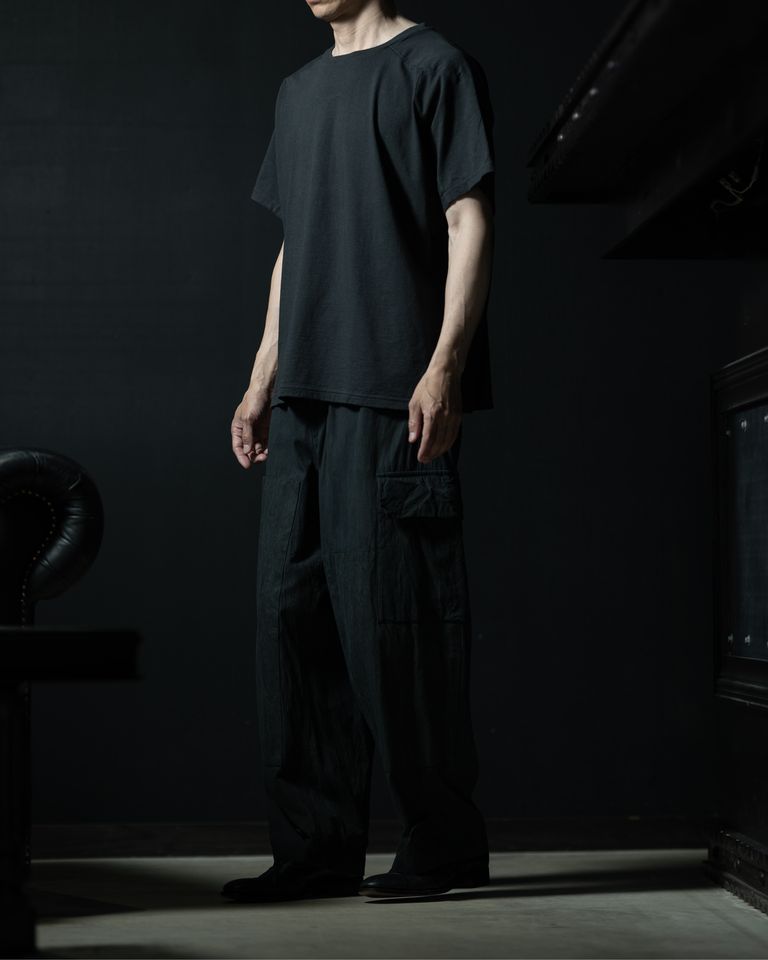 ドルマン調の袖によって横から見ると肩まわりに独特のボリュームが生まれ、通常のTシャツとは異なるシルエットのメリハリが確認できる。ワイドパンツの広がりと相まって、上下でバランスの取れたシルエットを形成している。