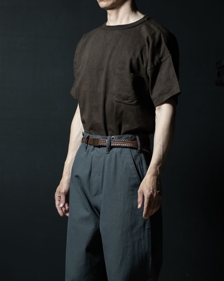 横からのタックインスタイル。インした裾がウエスト周りに自然なふくらみを作り、グレーパンツのハイライズラインを引き立てる。泥染め生地のドレープが光を受けて微妙な色変化を見せる。