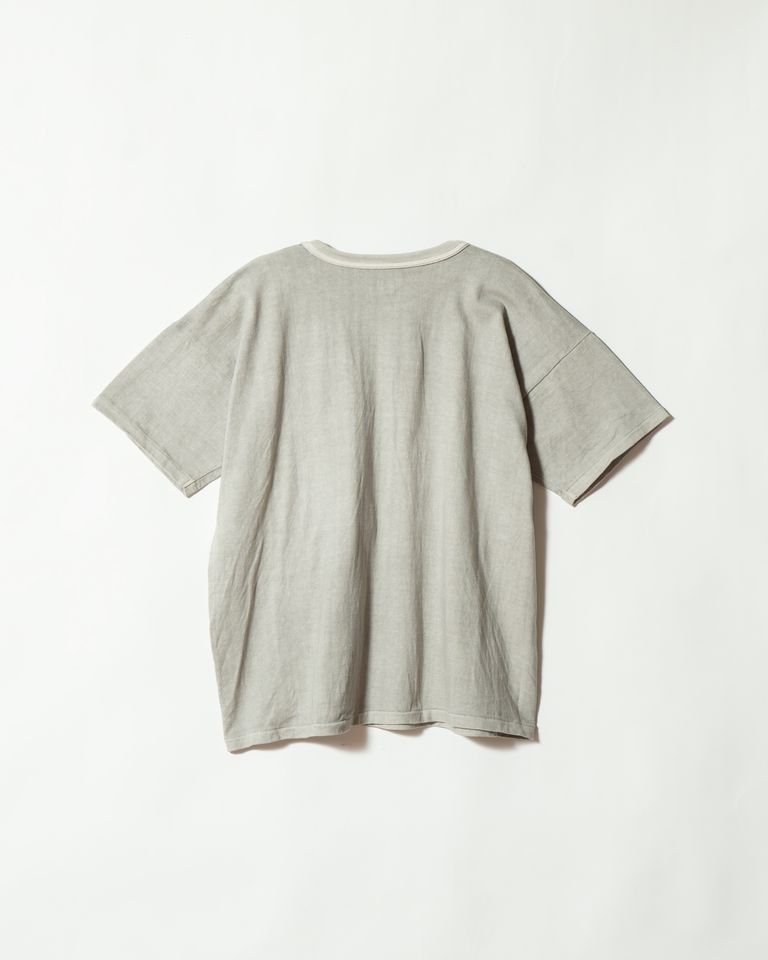 バックビューでは墨染めのグレーグリーンが全体に均一に広がりながらも、光の反射で微妙な濃淡が生まれているのが確認できる。生成りのネックリブが後ろ首元でさりげないアクセントとなり、一枚の完成度を高める。