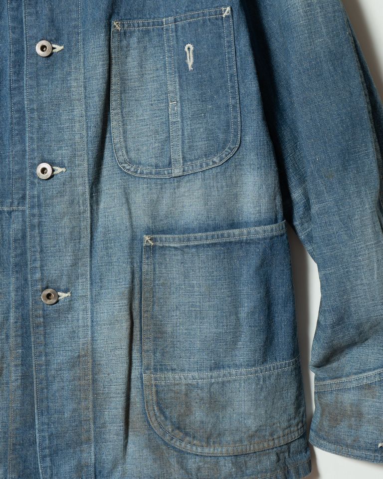 右前身頃のポケット詳細。縫い目の補強や意図的に再現されたほつれが、30年代ヴィンテージへの深いリスペクトを感じさせる。鉄製ボタンの刻印とざらついたテクスチャーが、経年変化への期待を搔き立てる。