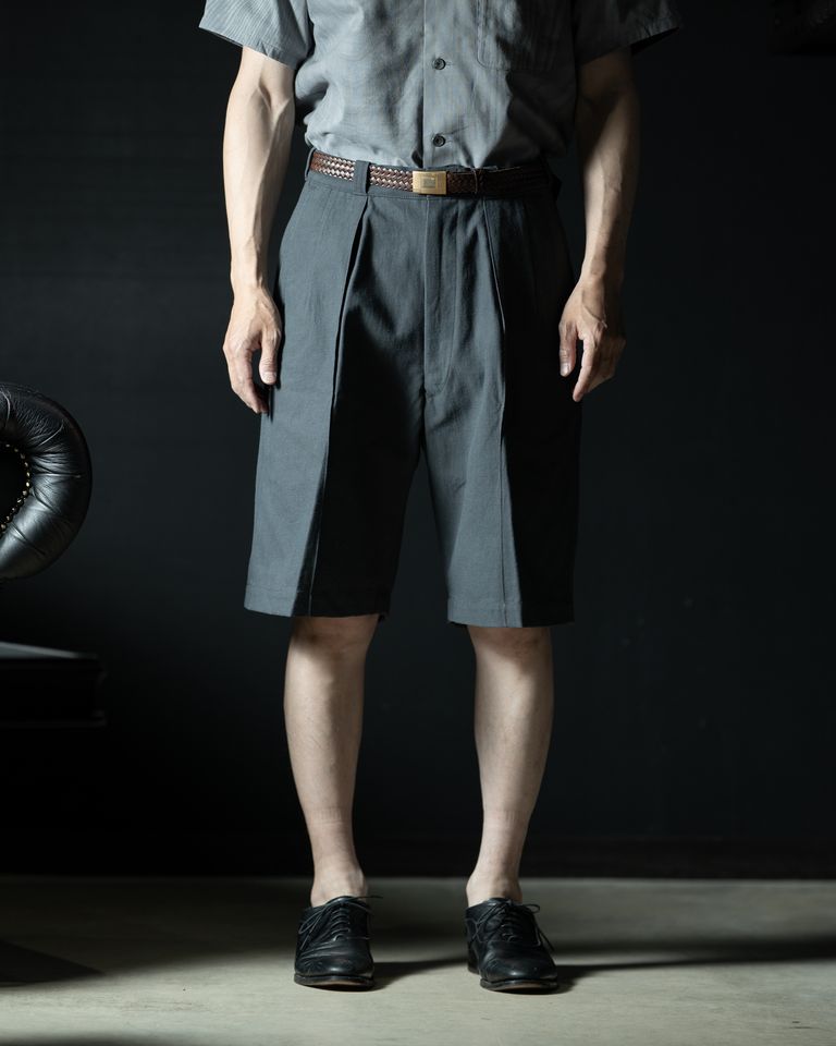 センタープリーツが美しく落ちる正面シルエット。2タックによる立体的なドレープが脚のラインをすっきりと見せ、ブラウンのメッシュベルトとの相性も抜群。スラックスのような上品さをショーツで体現している。