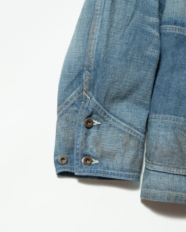 裾周りと袖付け根のディテール。肩線から袖山を一気に縫い上げる高度な技法による独特の造形と、未メッキ鉄製ボタンが醸す無骨な質感が間近で伝わる。オイル汚れのダメージ加工が、使い込まれた道具としての説得力を高める。