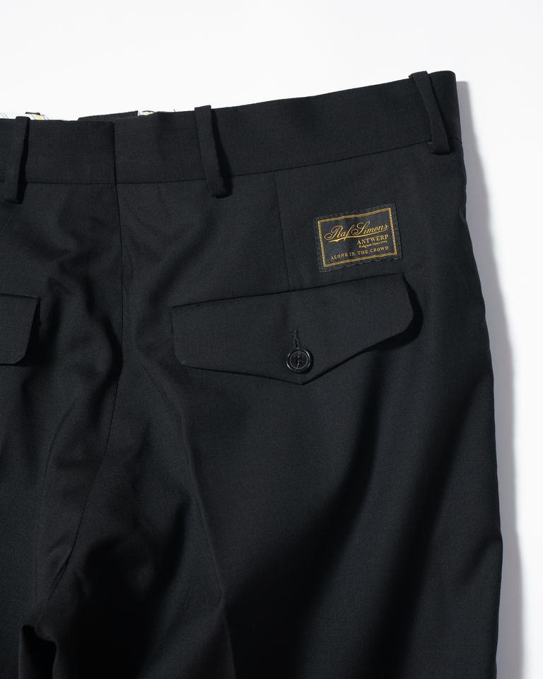 RAF SIMONSのクラシックストレートスラックスは、99%のラナヴァージンウールと1%のエラスタンを組み合わせた生地を使用しており、柔軟性と快適性が特徴です。イタリアで生産され、高品質が保証されています。このパンツは、クラシックなストレートシルエットでありながら、程よいワイド感が現代的な印象を与えます。ウエストバンドはフィット感を高め、穿き心地を向上させています。