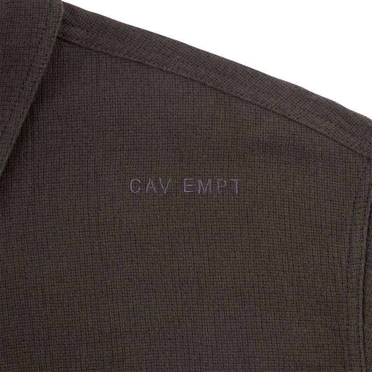 リネン混のワッフル織り生地のテクスチャクローズアップ。凹凸のある編み地が光を受けて陰影を作り、素朴でありながらも上質な表情を持つ。肩部分には「CAV EMPT」のトーンオントーン刺繍が施されており、さりげなくブランドを主張する。