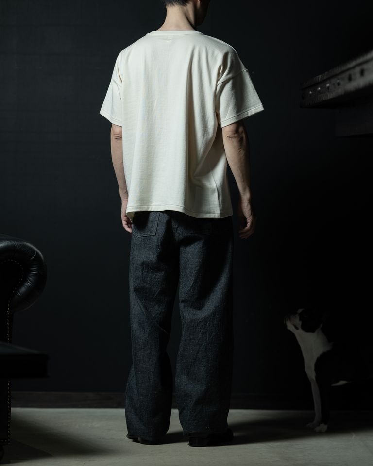 後ろ姿の全身カット。ワイドなデニムと合わさり、上下ともにたっぷりとしたボリュームが統一感を生む。右奥に佇む犬がスタイリングに自然な温度感を加える。