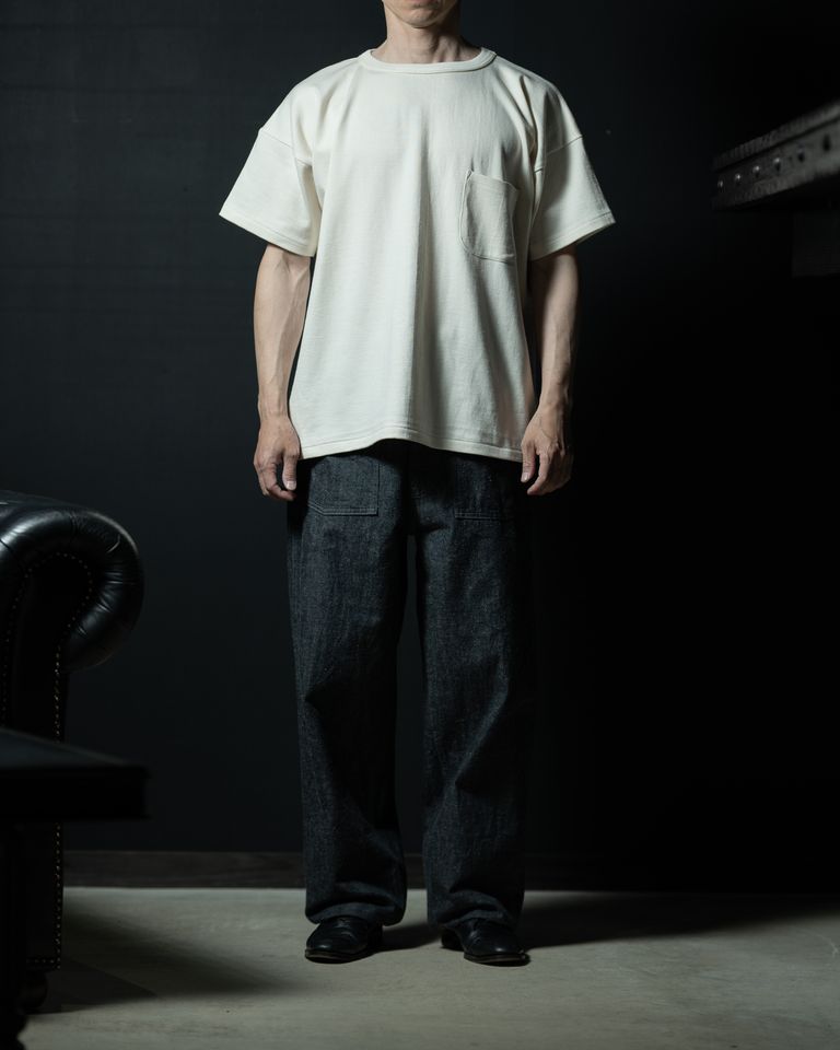 ワイドデニムとの組み合わせで完成するボリューミーなシルエット。Tシャツの裾が腰回りにかかるレングスが、抜け感と存在感を同時に演出。黒のレザーシューズが全体を引き締める。