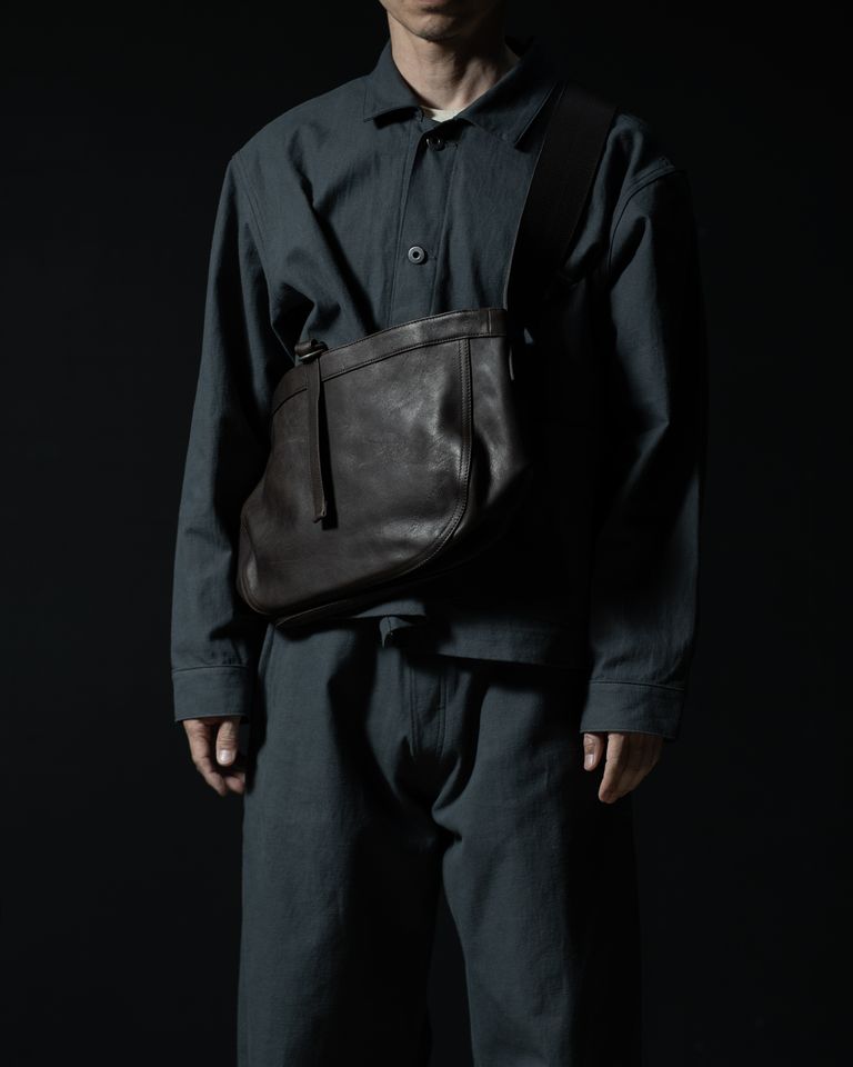 前掛けでのスタイリング例。身体にフィットするサイズ感と、象徴的なショルダーハンドルのディテールが際立ち、クラシックとモダンが交差する佇まいを演出します。