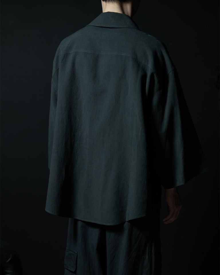 背面から見るとヨーク切り替えの位置と袖の付け幅が確認できる。肩線が意図的にドロップしており、コートの背中に近い直線的なシルエット。リネン×シルクの生地は光の方向で表情が変わり、暗所では重厚感が出る。