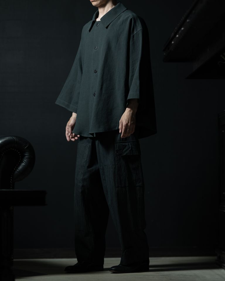 サイドから見ると着丈の前後差と裾のラウンドラインが明確になる。袖がドルマン気味に広がるため、腕を前に出すと袖の面積が変化し、動くたびに表情が変わる。パンツのカーゴポケットとの組み合わせで、全体に素材感で統一したミニマルな着こなし。