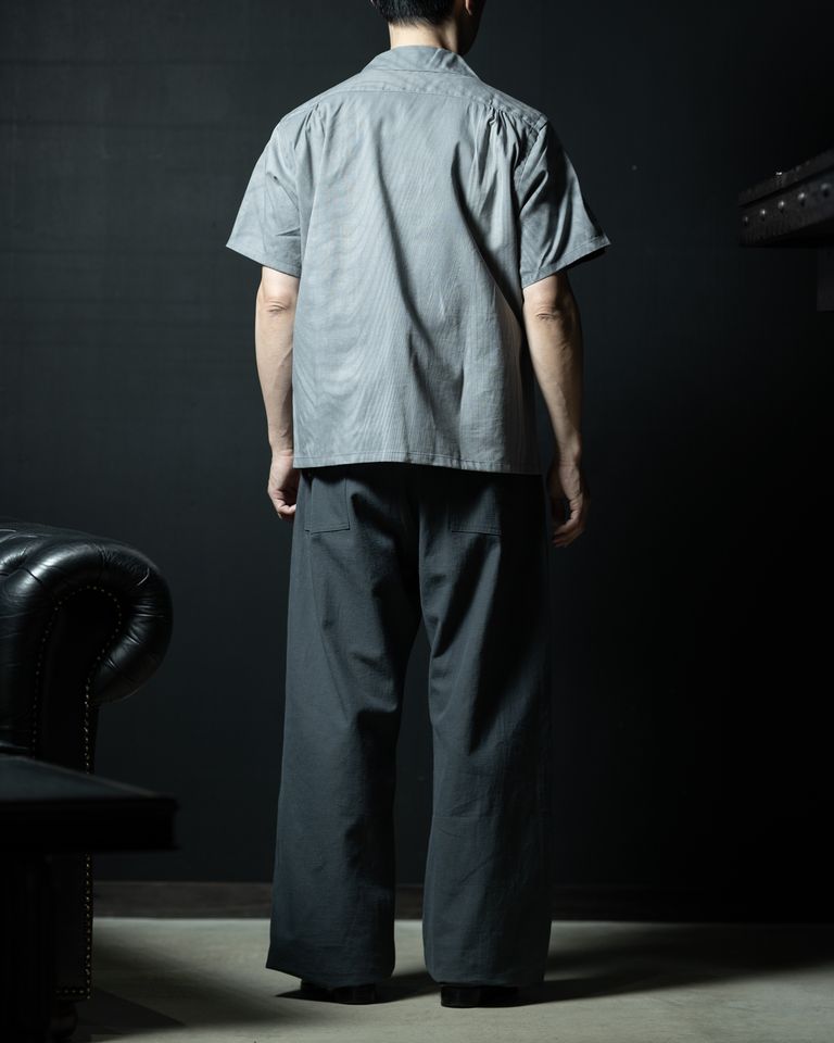 バックフルレングス。裾はストレートにカットされ、清潔感のある後ろ姿を演出。ワイドパンツとの組み合わせで、全体にゆとりのある立体的なシルエットが完成。左手側にはチェスターフィールドソファが見え、空間全体の雰囲気を高める。