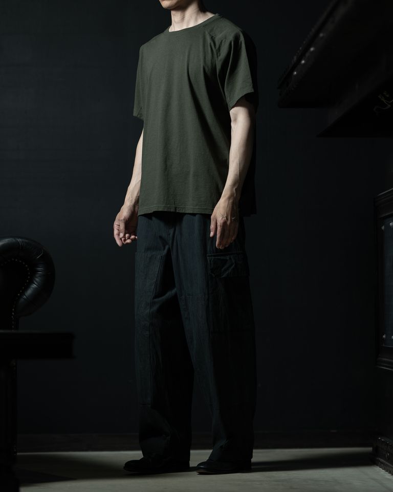 斜め前からの全身カット。ドルマン調の袖によって横から見ると肩まわりに独特のボリュームが生まれ、通常のTシャツとは異なるシルエットのメリハリが確認できる。ワイドパンツの広がりと相まって、上下でバランスの取れたシルエットを形成している。