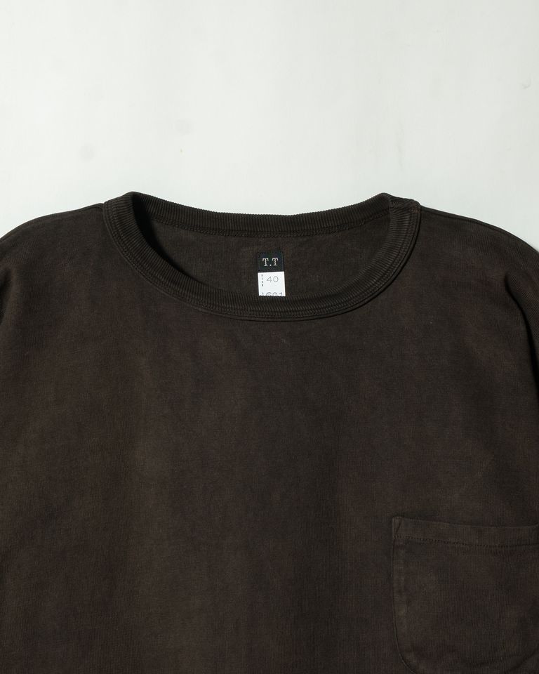 「T.T」タグとサイズ表記が入った首元のクローズアップ。二重仕立てのネックリブにも泥染めが深く浸透し、色の濃淡が生地の表情に溶け込む。染めムラが光によって微妙に変化し、豊かな陰影を生み出す。