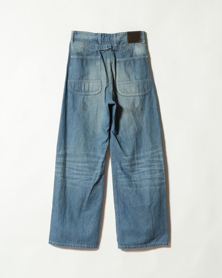 バックは大きなパッチポケットが左右に配置された、ワークウェアらしい実用的なデザイン。腰部のバックルベルトとブラウンレザーパッチが、後ろ姿に力強いアクセントを加える。