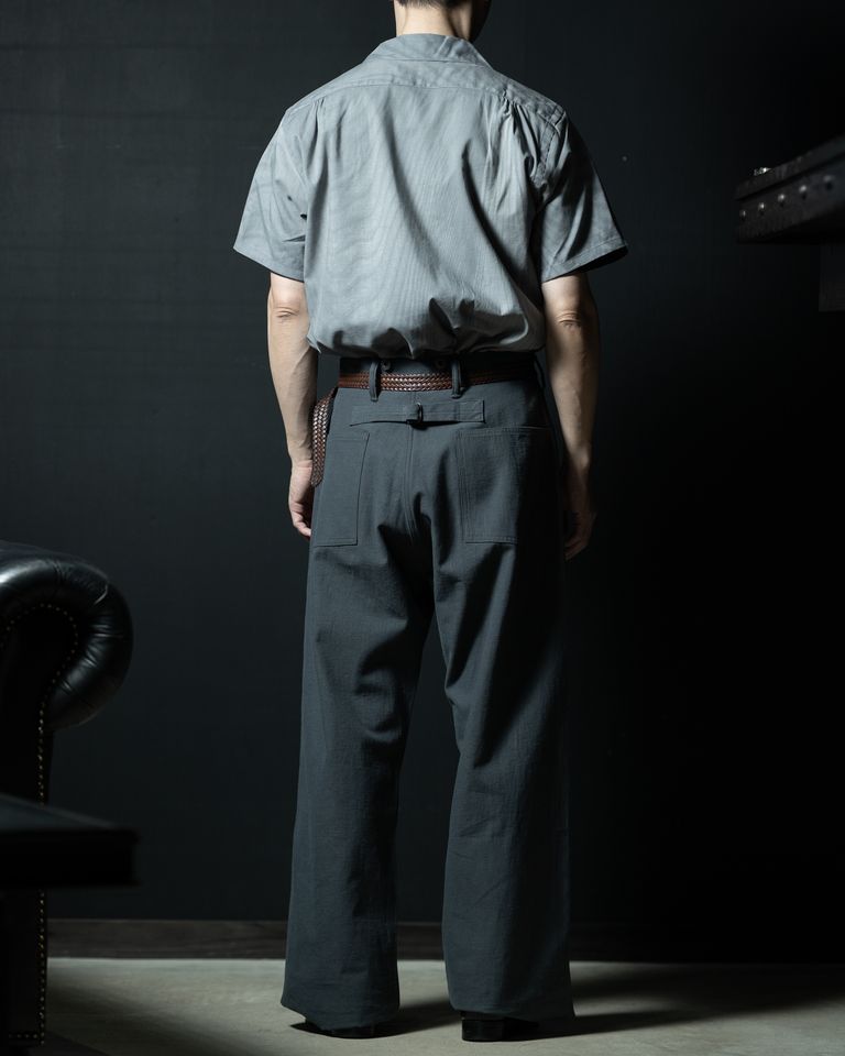 タックインのバックフルレングス。ワイドパンツとの組み合わせで、腰回りのゆとりと裾へのフレアが美しく展開する。バックポケットのパッチデザインが見え、パンツのディテールも確認できるスタイリングショット。