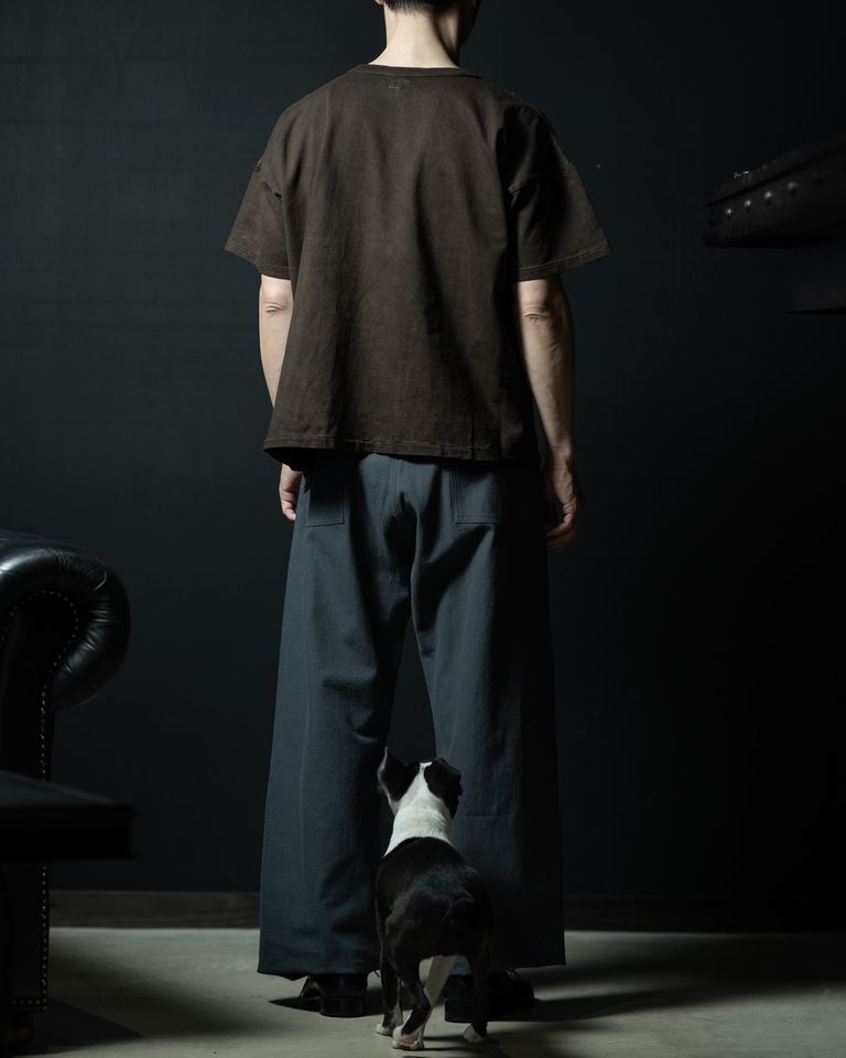 後ろ姿の全身カット。足元には愛犬が寄り添い、空間に生活感と温もりを添える。ダークブラウンとグレーの配色が後ろ姿にも統一感をもたらし、着こなし全体に静かな品格が漂う。