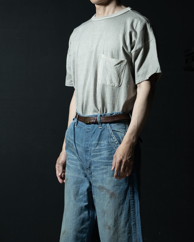 横からのタックインスタイル。インした裾がウエスト周りに自然なボリュームを生み、デニムのハイライズラインとブレイデッドベルトがシルエットを引き締める。墨染めのドレープが光を受けて豊かに変化する。