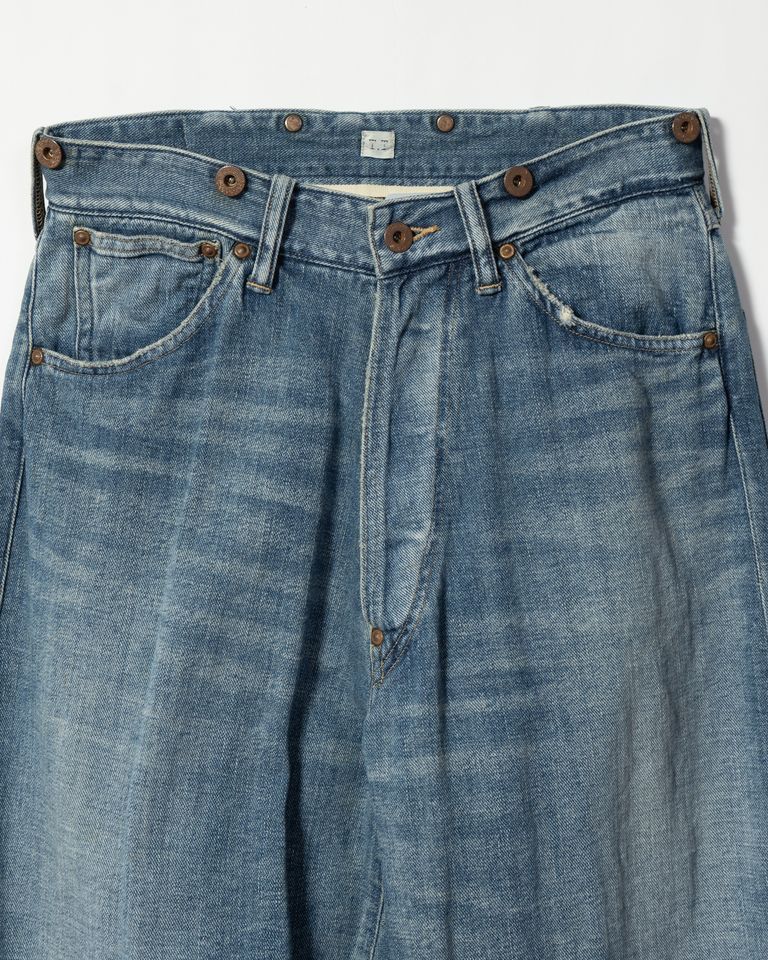 Taiga Takahashi のアイコニックアイテムでもある Lot.704 Demin Trousers c.1920s にダメージ加工を施したジーンズ。通常のダメージ加工に加え。塩縮加工を施すことで、生から穿いたような、シワ、ヒゲ等のユーズド感を実現した。錆びて朽ちたボタンとリベット、バックルが存在感を作り出している。