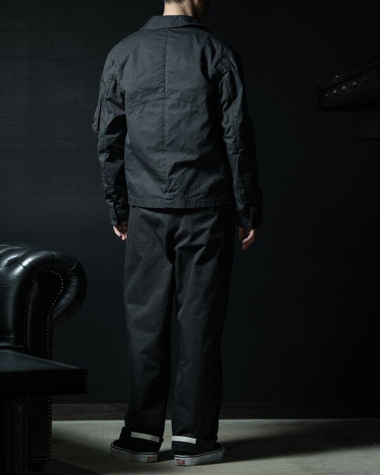 背面から見ると、肩から裾へと緩やかに落ちる立体的なラインが際立ちます。軽やかなFINXギャバジンが身体の動きに合わせて自然な表情を生み、ミリタリー由来の構造と端正なバランスが調和したデザインです。